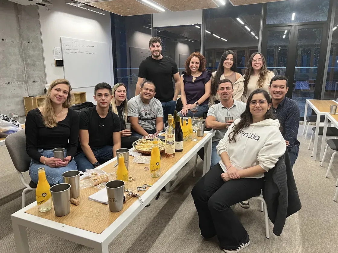 Environ onze membres de l'équipe Eventtia autour d'une longue table de bureau en soirée, verres sortis, une personne en hoodie eventtia.