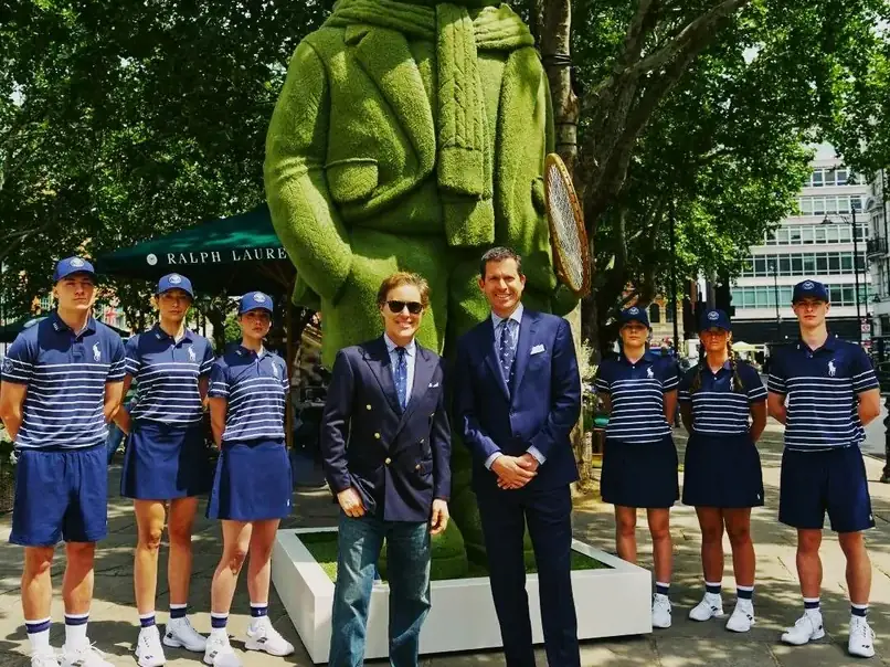 Activation Summer of Sport de Ralph Lauren à Sloane Square, Londres : deux hommes en costume Ralph Lauren devant un Polo Bear géant en topiaire habillé pour le tennis, entourés de six membres du staff Polo Ralph Lauren en uniforme marine.