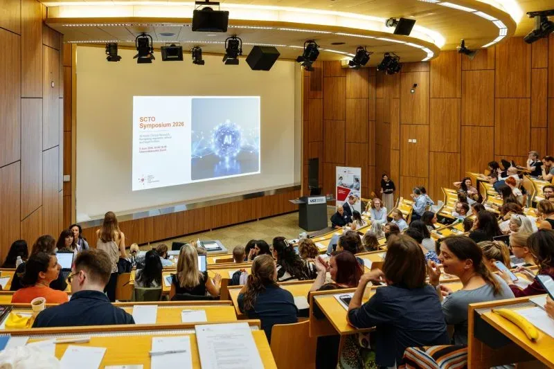 Auditorium plein au SCTO Symposium 2026, avec une diapositive projetée « SCTO Symposium 2026 ».