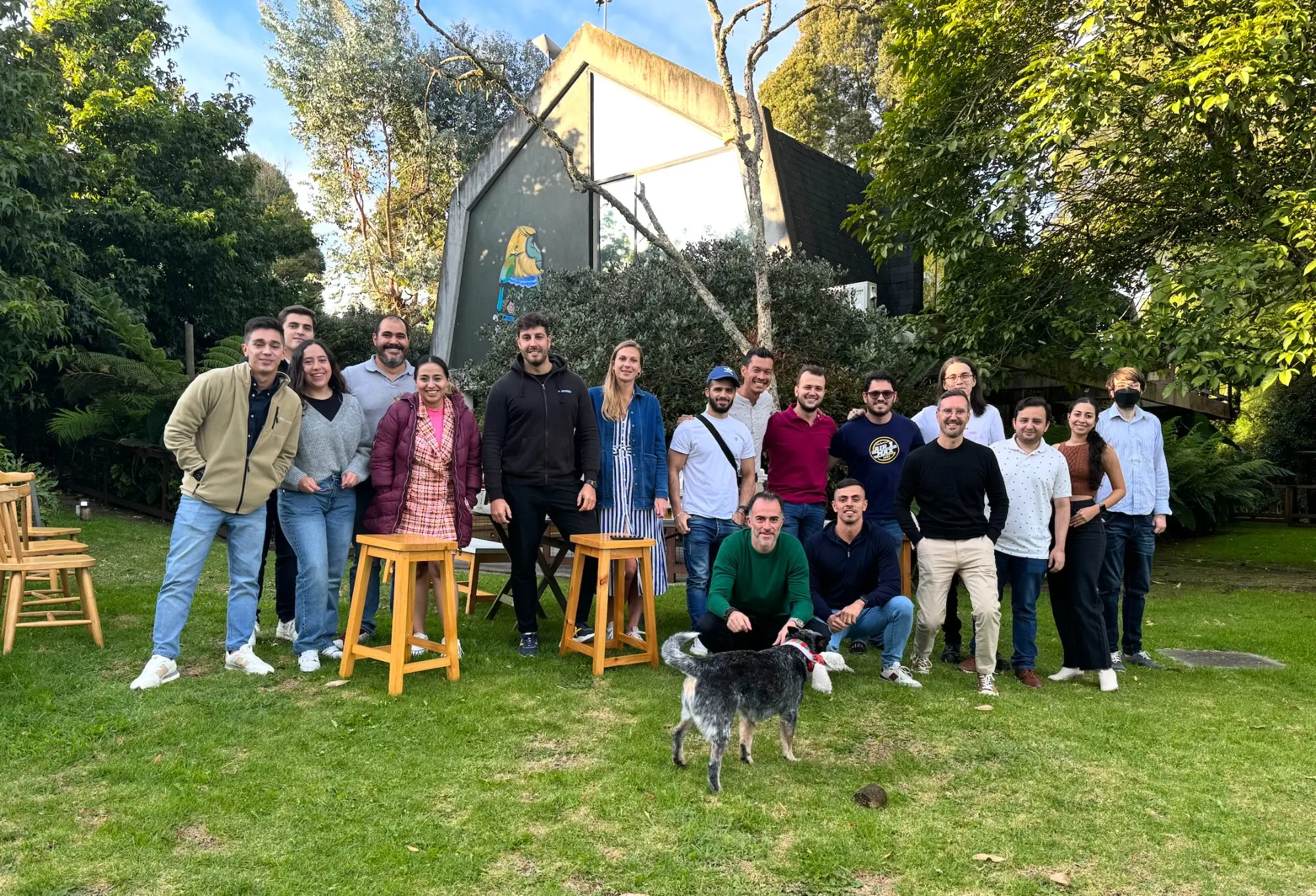 L'équipe Eventtia réunie en plein air lors d'un rassemblement d'équipe, autour de tabourets sur la pelouse, avec un chien au premier plan.