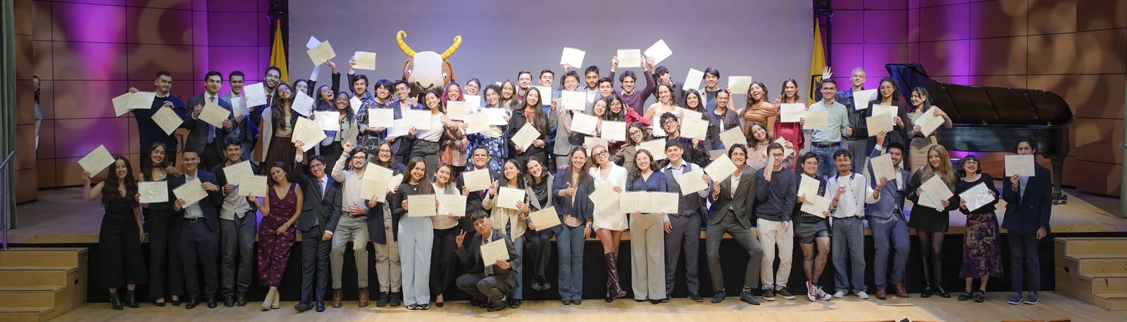 Estudiantes de la Universidad de los Andes en el escenario con sus certificados durante una ceremonia